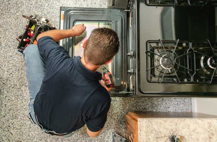 A technician fixes an oven in a kitchen, highlighting a kitchen appliance repair service in Henderson, NV.