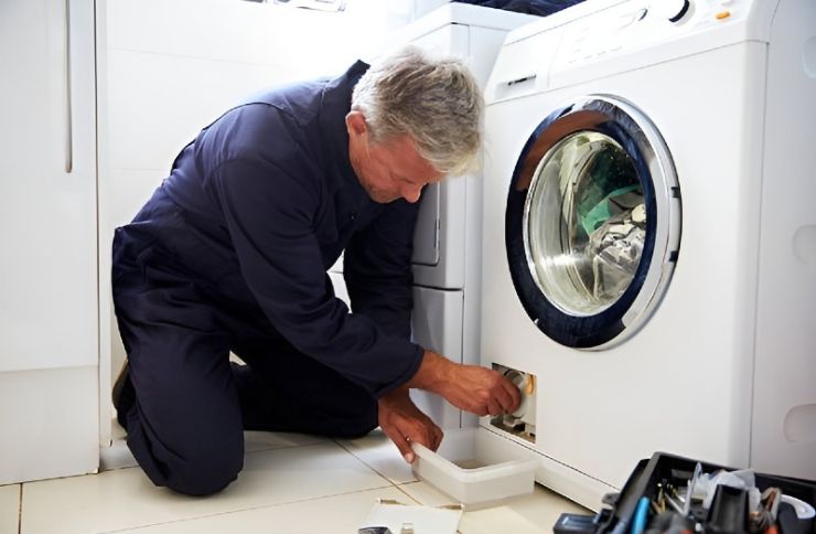 A man works on a washing machine in a bathroom, highlighting a laundry appliance repair service in Henderson, NV.