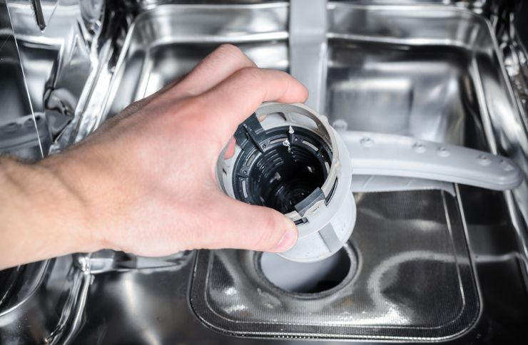 A person is cleaning a dishwasher with a drain plug, illustrating appliance repair services available in Henderson, NV.