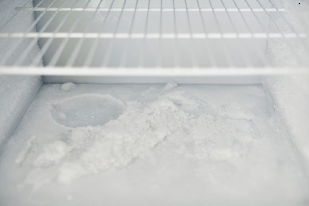 A white refrigerator filled with ice, emitting an unpleasant odor.