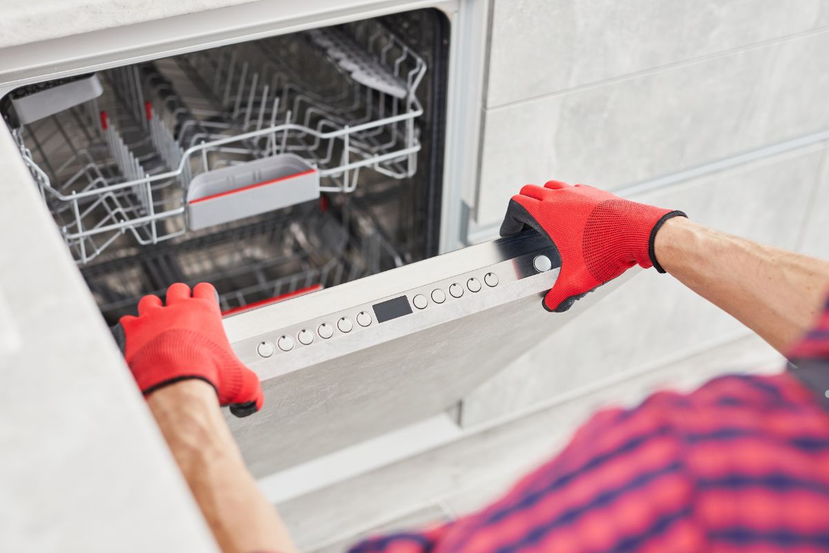 A man in red gloves holds a dishwasher, representing an appliance repair service in action.